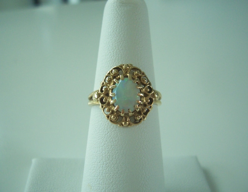 May include: A gold ring with an oval opal gemstone set in a filigree design.