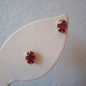 May include: A pair of gold earrings with red oval-shaped gemstones.