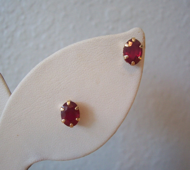 May include: A pair of gold earrings with red oval-shaped gemstones.