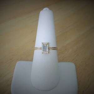 May include: A gold engagement ring with a large emerald cut diamond and a band of smaller diamonds.