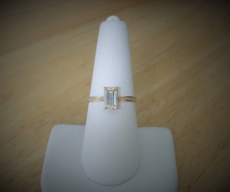 May include: A gold engagement ring with a large emerald cut diamond and a band of smaller diamonds.