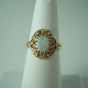 May include: A gold ring with an oval opal gemstone set in a filigree design.