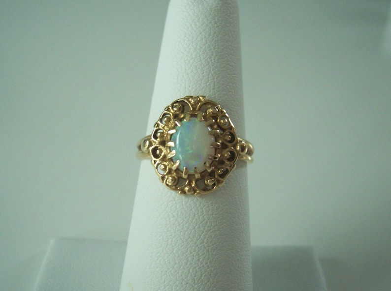 May include: A gold ring with an oval opal gemstone set in a filigree design.