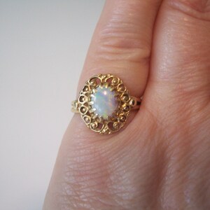 May include: A gold ring with an oval opal gemstone set in a filigree design.