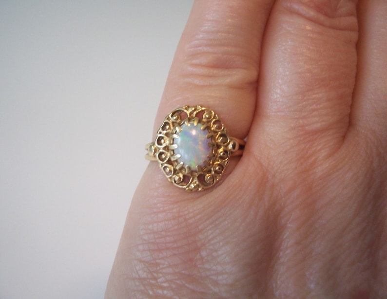 May include: A gold ring with an oval opal gemstone set in a filigree design.