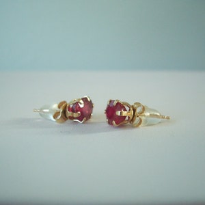 May include: A pair of gold earrings with red gemstone accents. The earrings have a simple design with a small, round gemstone set in a gold setting.