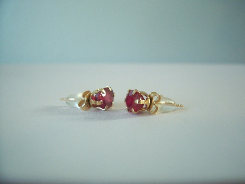 May include: A pair of gold earrings with red gemstone accents. The earrings have a simple design with a small, round gemstone set in a gold setting.