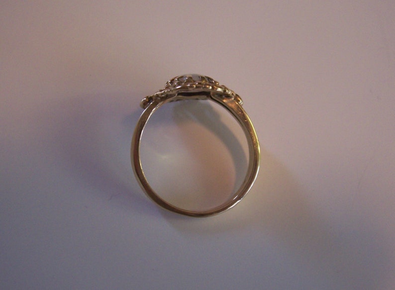 May include: A gold ring with a white stone set in a decorative design.