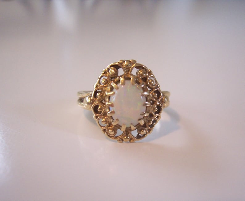 May include: A gold ring with an oval-shaped opal gemstone set in a delicate filigree design.
