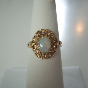 May include: A gold ring with an oval opal gemstone set in a filigree design.
