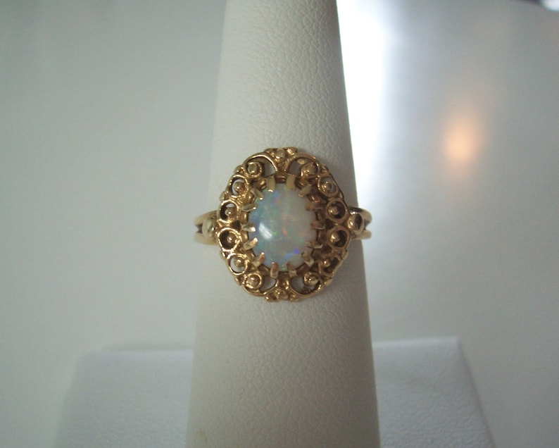 May include: A gold ring with an oval opal gemstone set in a filigree design.