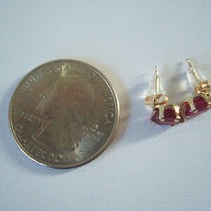 May include: A pair of gold stud earrings with red gemstone accents. The earrings are shown next to a US quarter for size comparison.