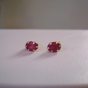 May include: A pair of gold earrings with oval-shaped ruby gemstones.