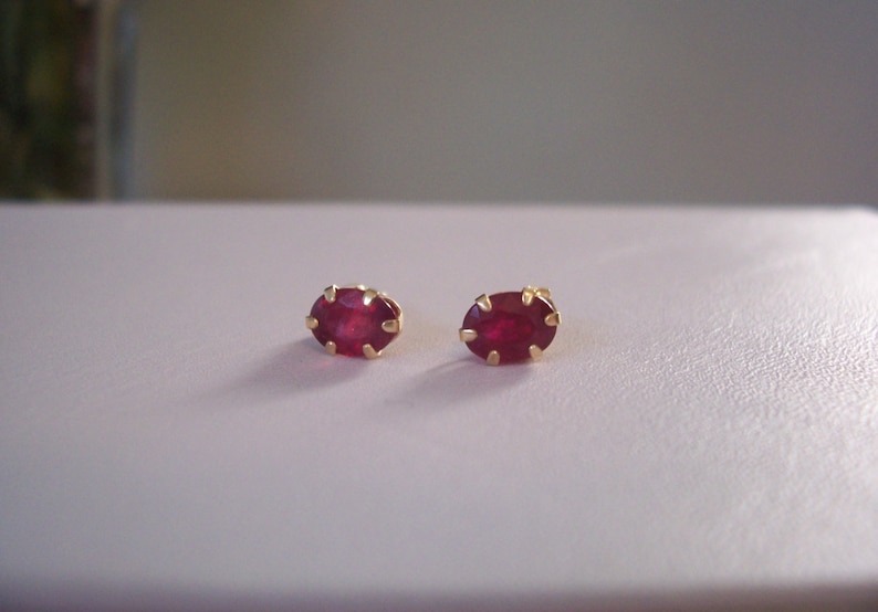 May include: A pair of gold earrings with oval-shaped ruby gemstones.