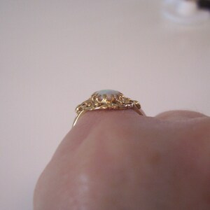 May include: A gold ring with a white opal gemstone set in a delicate filigree design.