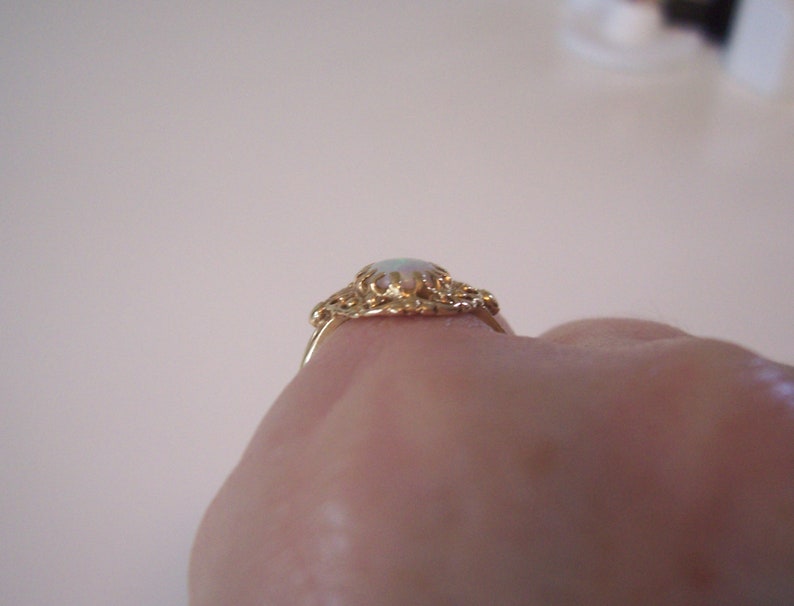 May include: A gold ring with a white opal gemstone set in a delicate filigree design.