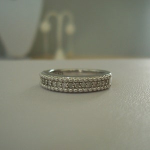May include: A silver band ring with a row of small diamonds set in a beaded design.