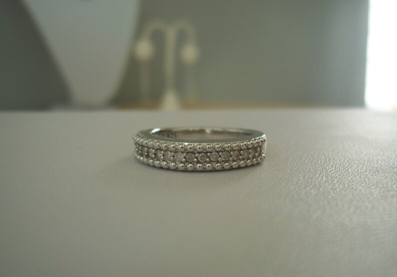 May include: A silver band ring with a row of small diamonds set in a beaded design.