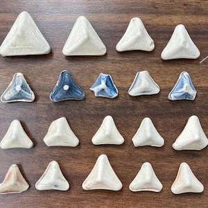 以下が含まれることがあります： 青と白のさまざまなデザインが施された、セラミック製の三角形のタイル20枚のセット。タイルは木製の表面に並べて配置されています。