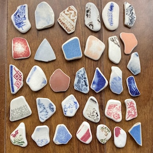 May include: An assortment of ceramic fragments, each with unique patterns in blue, red, and white, arranged on a wooden surface. The pieces vary in shape and size, offering a diverse range of designs and textures.