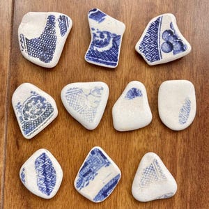 May include: Ten irregularly shaped, white ceramic pieces with blue floral and geometric patterns. The pieces vary in size and shape, arranged on a wooden surface. Each piece has a unique design.