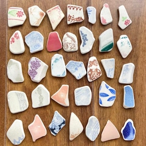 May include: A collection of irregularly shaped ceramic pieces with floral and geometric patterns in pink, blue, green, and brown. The pieces are arranged on a wooden surface, showcasing their unique shapes and designs.