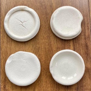 Może przedstawiać: Biały ceramiczny kubek z czarnym uchwytem i napisem "But First, Coffee" czarną, pogrubioną czcionką. Kubek stoi na drewnianej powierzchni. Kubek ma około 10 cm wysokości.