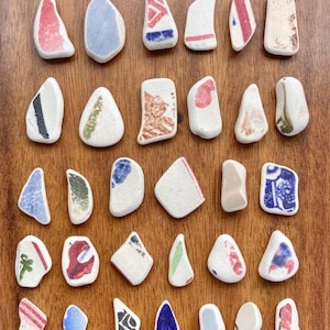 May include: A selection of small, irregularly shaped ceramic fragments with colourful patterns. The pieces display a variety of colours, including red, blue, green, and brown, against a white backdrop. The fragments are arranged on a wooden surface.