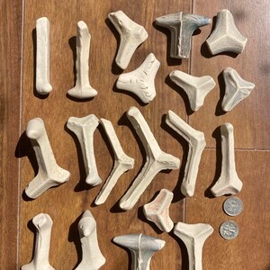 Könnte beinhalten: Eine Sammlung von cremefarbenen, abstrakten Keramikskulpturen in verschiedenen Formen, darunter T-Formen, Y-Formen und eckige Formen. Die Stücke sind auf einer Holzoberfläche mit einem Lineal in Zentimetern angeordnet.