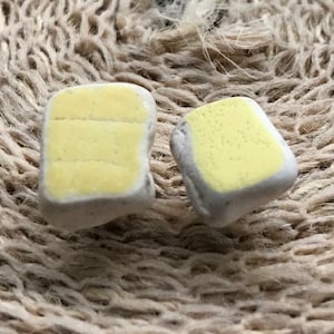May include: Two small ceramic tiles with a yellow glaze. One tile has a smooth surface and the other has a textured surface.