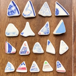 May include: A collection of small, triangular ceramic pieces with various blue and white patterns. Some triangles have floral designs, while others feature abstract patterns. The pieces are arranged on a wooden surface.