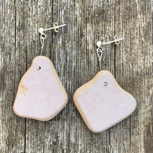 May include: A pair of pink ceramic earrings with silver posts. The earrings are irregular in shape and have a matte finish.