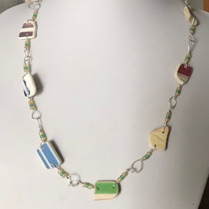May include: A silver chain necklace with colorful ceramic tile pendants. The tiles are in various shapes and sizes, including squares, rectangles, and irregular shapes. The tiles are decorated with stripes, dots, and other patterns.