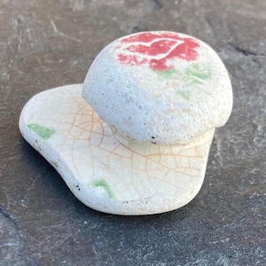 Puede incluir: Figurita de cerámica blanca en forma de hongo con un diseño de flor roja y verde en la parte superior. El hongo tiene un esmalte craquelado y una superficie texturizada.