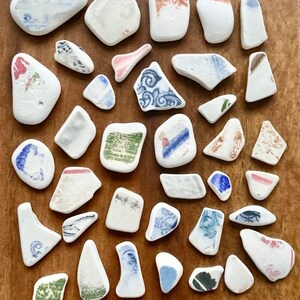 May include: A collection of white ceramic tiles with various blue, green, and red patterns. The tiles are arranged in a grid pattern on a wooden surface.