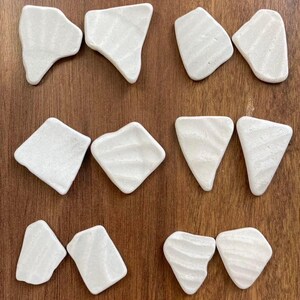 May include: Nine white ceramic dishes of various shapes and sizes. The dishes have a textured surface and are arranged in three rows of three.