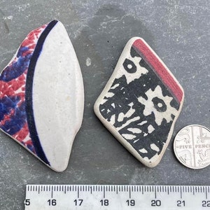 May include: Two pieces of ceramic pottery with unique patterns. One is white with red and blue designs, the other is a diamond shape with black and white patterns and a red border. A five pence coin is next to the pottery.