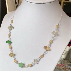 May include: A silver chain necklace with green, brown, and clear glass beads. The necklace is on a white mannequin.