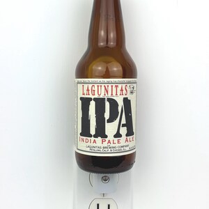 May include: A brown glass bottle of Lagunitas IPA beer with a gold cap, plugged into a white electrical outlet.