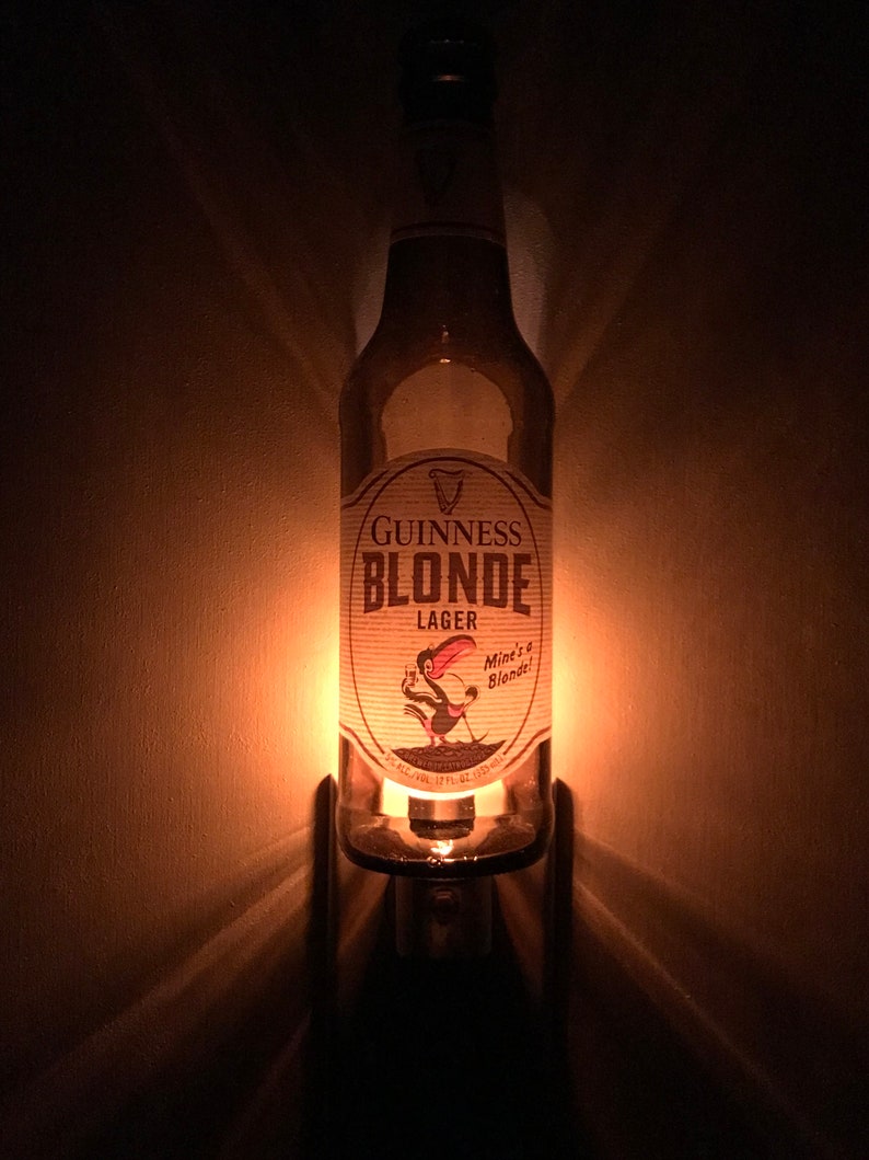 May include: A glass bottle night light shaped like a Guinness Blonde Lager beer bottle. The bottle has a white label with the text "Guinness Blonde Lager" and a cartoon bird with the text "Mine's a Blonde!"