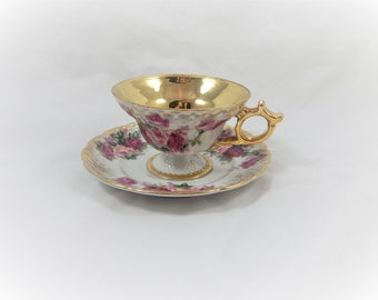 May include: A white teacup and saucer set with a gold rim and floral design. The cup has a gold interior and a gold handle. The saucer has a scalloped edge.