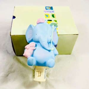 May include: A blue ceramic night light shaped like an elephant holding a pink bunny and an umbrella. The night light has a switch on the bottom.
