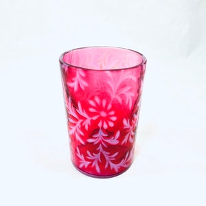 May include: A red glass tumbler with a white floral pattern. The glass is clear and has a smooth surface.