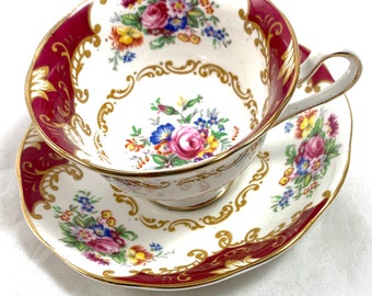 May include: A vintage teacup and saucer set with a white background and a red and gold floral pattern.