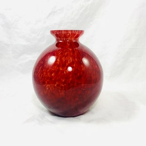 Może przedstawiać: Runda, czerwona szklana wazon z marmurkowym, nakrapianym wzorem. Wazon ma szeroki otwór i wąską szyjkę.