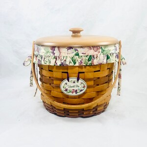 May include: A woven wood basket with a floral fabric lining and a wooden lid. The basket has two handles and a tag that says "Sweet Pea".