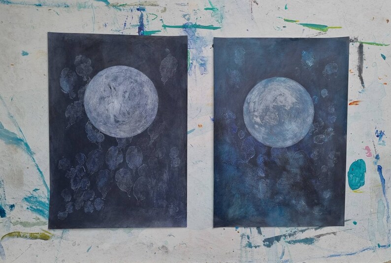 May include: Two abstract paintings of a white moon on a dark blue background. The moon is surrounded by white shapes that resemble leaves or clouds.