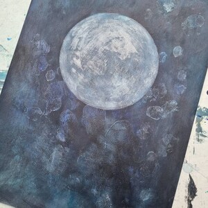 May include: A white moon painted on a dark blue background with white and blue splatter paint.