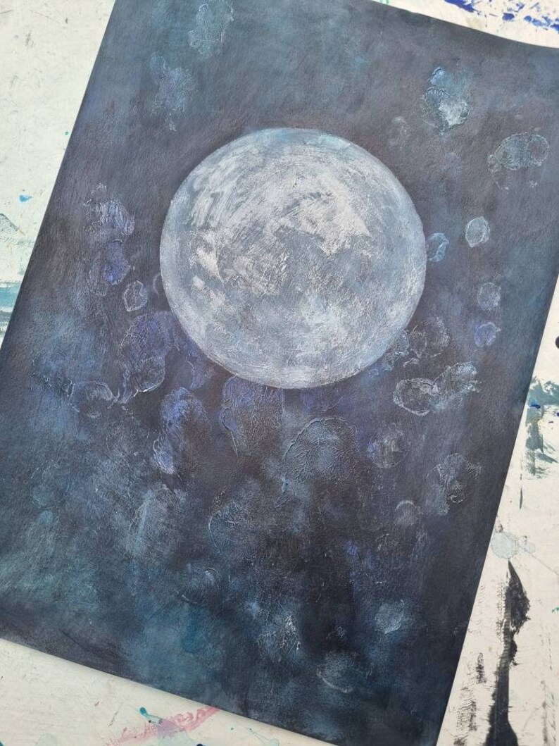 May include: A white moon painted on a dark blue background with white and blue splatter paint.
