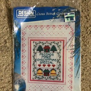 May include: Cross stitch pattern featuring a Christmas scene with houses, trees, and bells. The text reads "Friends Make Christmas Special".